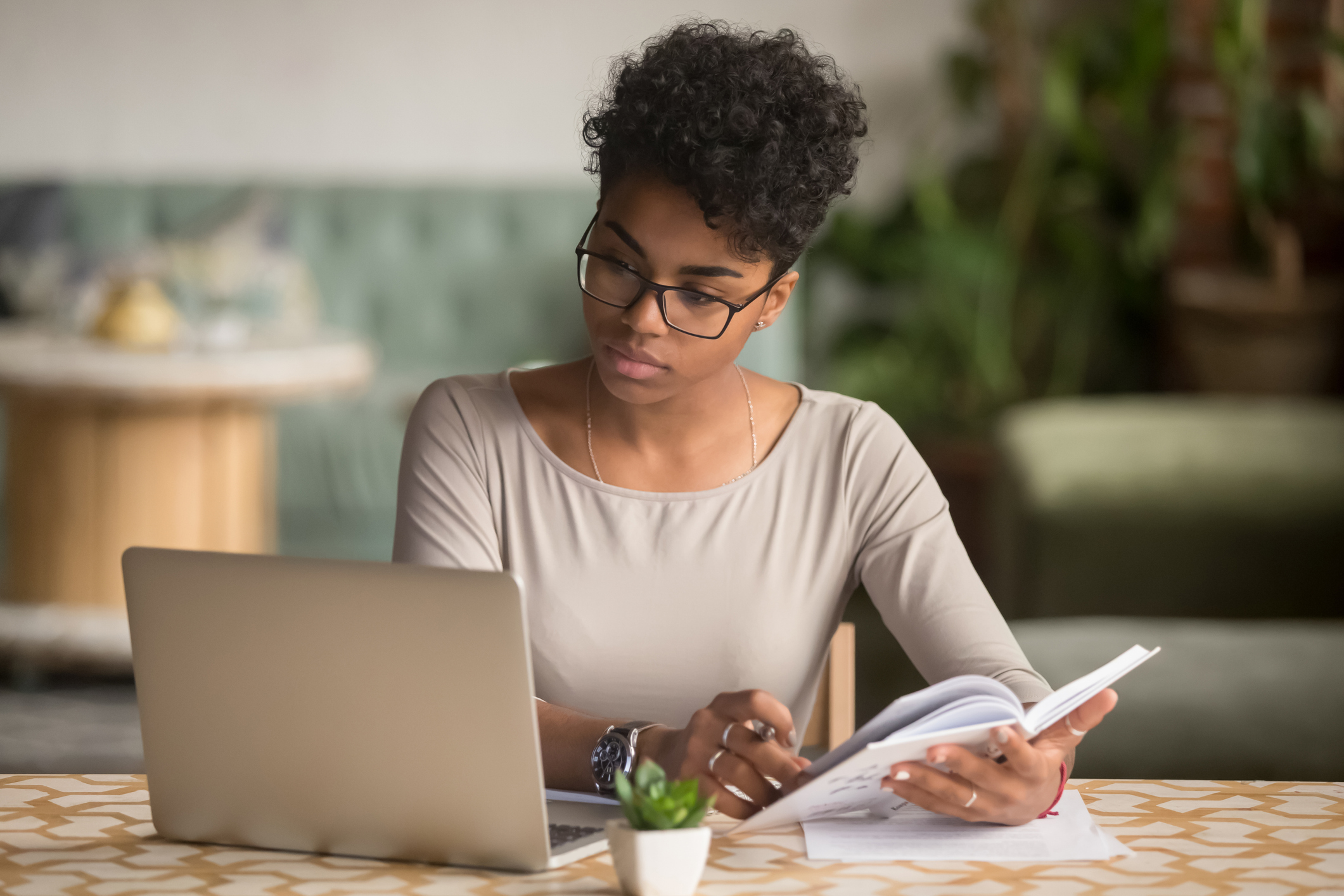 Focused african student looking at laptop holding book doing research Focused african student looking at laptop holding book doing research