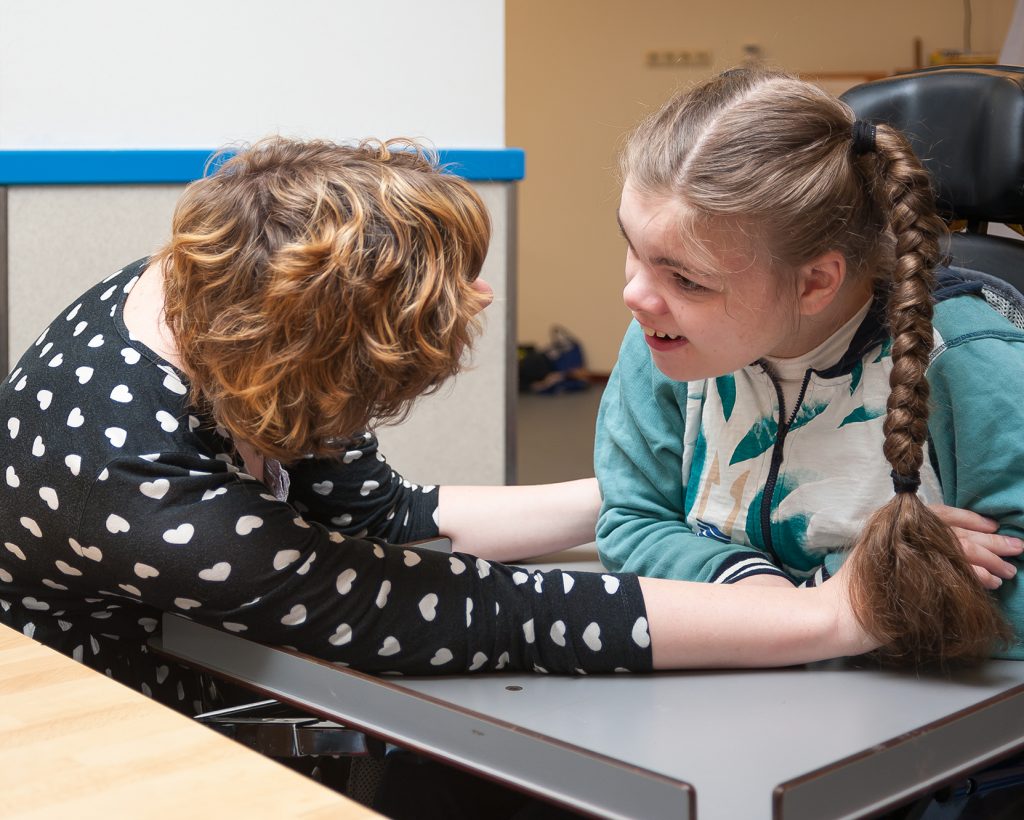A disabled child in a wheelchair making eye contact with a special needs carer
