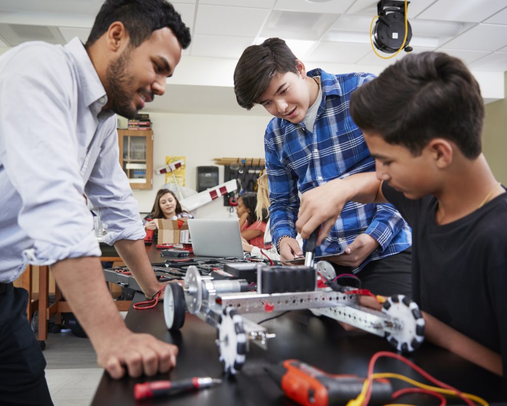 Teacher With Male Pupils Building Robotic Vehicle In Science Lesson